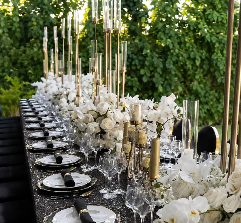 Table de mariage dressée avec vaisselle noir et or et compositions florales blanches